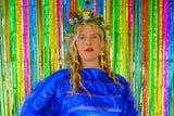 Close-up of Model with blonde hair and a headdress wearing a RAZZLE DAZZLE tinsel tassel kaftan maxi dress with sheer mesh panels. 