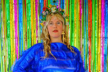 Close-up of Model with blonde hair and a headdress wearing a RAZZLE DAZZLE tinsel tassel kaftan maxi dress with sheer mesh panels. 