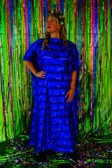 Model with blonde hair and a headdress wearing a RAZZLE DAZZLE tinsel tassel kaftan maxi dress with sheer mesh panels. The showstopping dress features shimmering tassels, a loose fit, and a slash neck. It can be worn free-flowing or cinched with hidden ribbons for a more fitted silhouette. Made from limited deadstock fabric, the semi-sheer dress is paired with just a bra and knickers in this photo, perfect for the festive season.