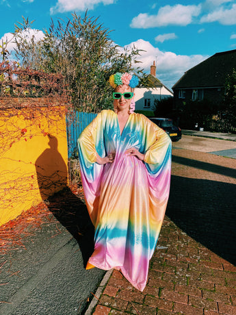 Model wearing a shimmering, liquid holographic maxi kaftan dress in pastel rainbow colors.