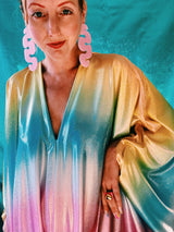 Close-up of model wearing a shimmering, liquid holographic maxi kaftan dress in pastel rainbow colors.