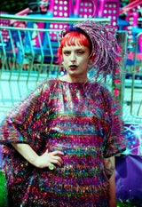 Close-up of the model wearing the TINSEL Maxi Black and Multicoloured Shimmer kaftan Dress at the funfair with one hand on hip